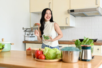 Portrait of pretty young woman eating fresh salad from in modern kitchen. Wellbeing and healthy lifestyle concept