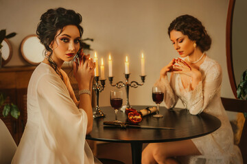 Art portrait real people two women Sexy girl beauty face lips sitting at the dinner table luxury light room. vintage nightie silk white long dress fairy old style noble lady girls. red wine glasses