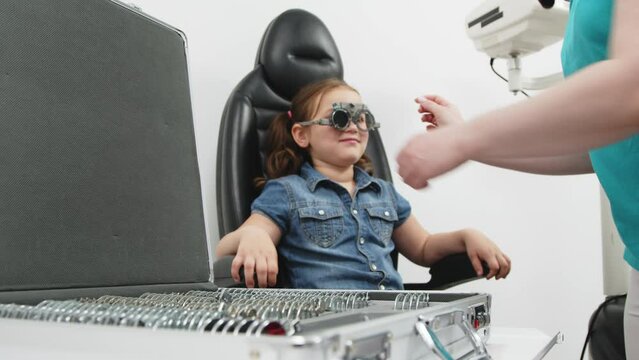 A female doctor holds special glasses to a patient for eye examination and lens selection in the clinic. Ophthalmology concept. An optician checks the vision of a small child.