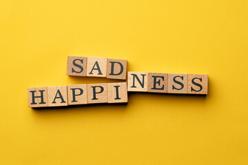 a yellow warm background without shadows wooden cubes with black letters laid out word happiness sadness