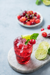 Cherry-lime mojito cocktail with mint, lime and ice on a marble board on a light  background.