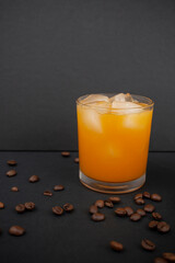 Orange juice with ice cubes in a glass and scattered coffee beans on black