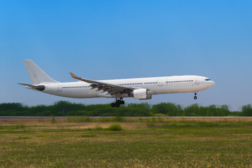 A large white passenger airliner landing on a sunny summer day against the backdrop of a green forest and a cloudless blue sky. Side view. Motion blur in the background