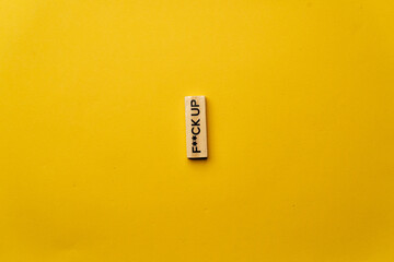 a yellow warm background without shadows wooden cubes with black letters laid out word fuck up