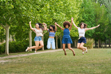 Four young women are jumping in the air in a park