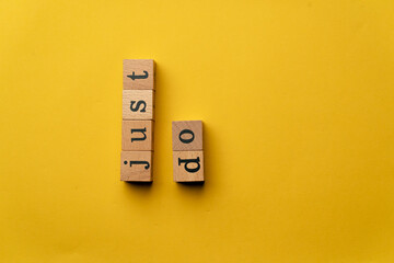 a yellow warm background without shadows wooden cubes with black letters laid out word just do