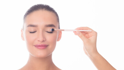 A woman is holding a brush and skillfully applying eyeliner to her eyelids. The focused look on her face shows precision and concentration in the makeup application process.