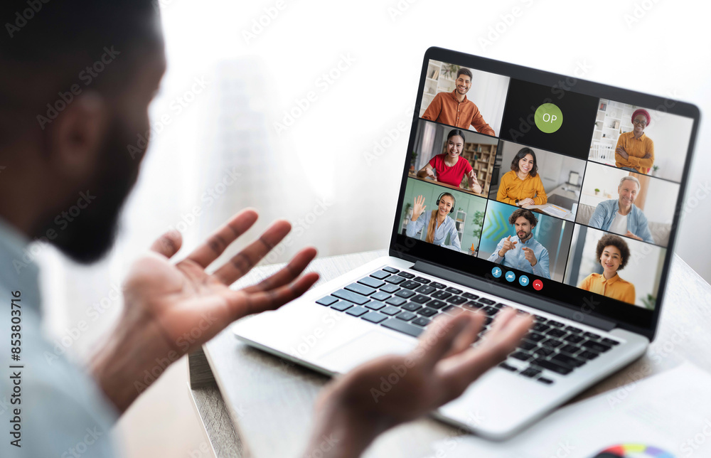 Aufkleber Black man sits in front of a laptop, participating in a video conference meeting with several colleagues. He has his hands raised as if he is making a point during the call.