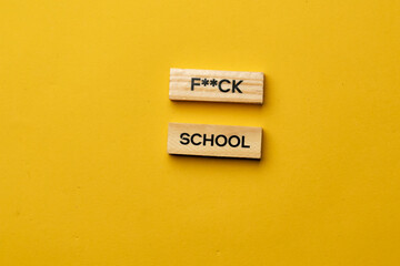 a yellow warm background without shadows wooden cubes with black letters laid out word fuck school