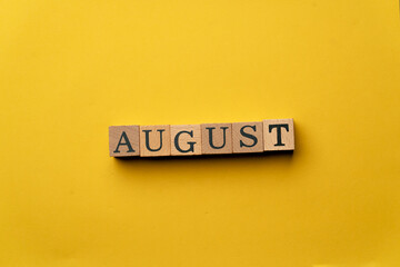 a yellow warm background without shadows wooden cubes with black letters laid out word august