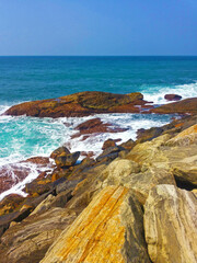 A rocky seashore with waves crashing against the rocks under a clear blue sky