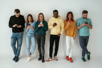 Fototapeta premium Busy by using smartphones. Group of young people are standing against white background
