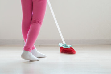 Child using red small broom with white plastic stick and sweeping light laminate floor at home...