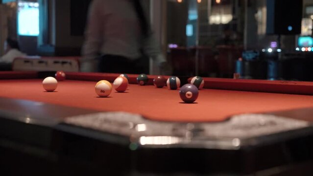 A billiard player hits a ball with a cue stick on an orange table in a sports pub and hits the pocket close-up