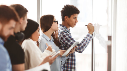 Students writing algebra equations on whiteboard, studying in college classroom