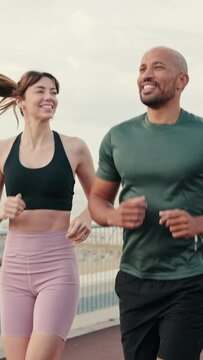 Close-up side view of young couple of athletes wearing sportswear running on the seafront outdoors