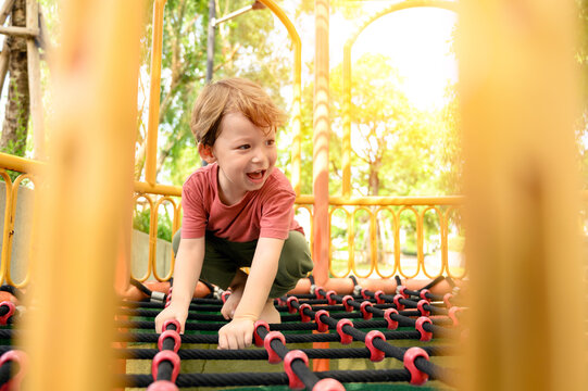 cute little boy climbing on net robes on playground in schoolyard. happy and enjoy adventure sports play alone outdoor playground.