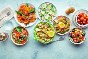 Fresh salads, overhead flat lay shot of an assortment. Variety of plates and bowls with green vegetables. Healthy food, top shot, on a slate background