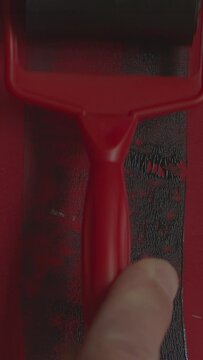 hand holding a red paint roller, black lino ink remain, linocutting paint roller texture on red photo paper background, 9x16 asset.