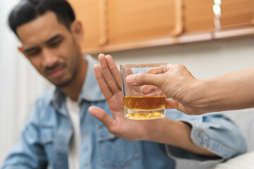 Alcoholism, depressed asian young man refuse, push out alcoholic beverage glass, drink whiskey, sitting alone at night. Treatment of alcohol addiction, having suffer abuse problem alcoholism concept.