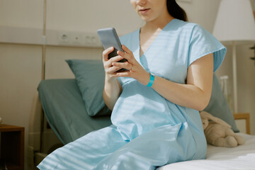 Young pregnant woman texting via mobile phone while she sitting in ward