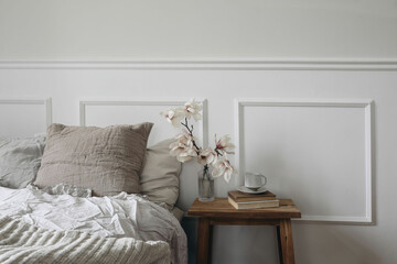 Elegant bedroom. Wooden night stand with fluted glass vase. Blooming magnolia tree branches. Cup of...