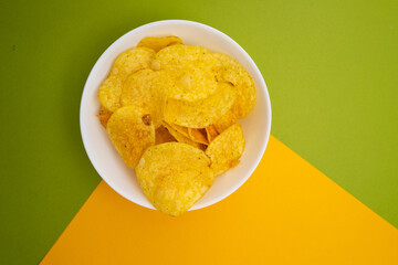 Crispy potato chips in a bowl close-up on a colored background. Colors and diet. Quick snack. Place for text