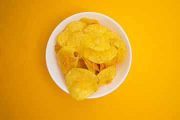 Crispy potato chips in a bowl close-up on a colored background. Colors and diet. Quick snack. Place for text