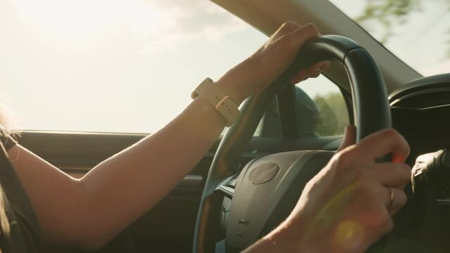 Close up view of female driver hands on steering wheel. Woman driving car at sunset. Inside view of modern vehicle moving on road