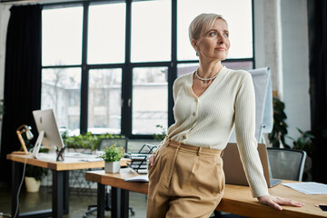 A middle-aged businesswoman with short hair is focused on work at a desk in a modern office setting.