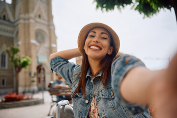 Young carefree woman taking selfie while traveling and looking at camera.