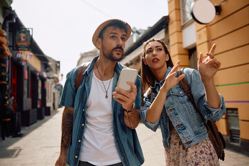 Young woman showing direction to  tourist who is using cell phone while walking in  city.