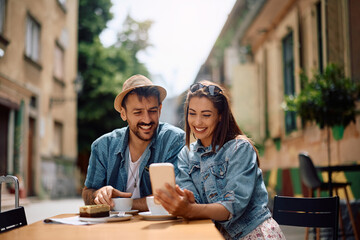 Happy couple having cup of coffee while using mobile phone in sidewalk cafe.