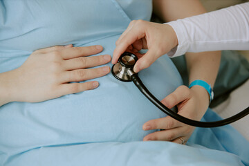 Medium close up of pregnant woman holding her belly while obstetrician checking heartbeat of fetus