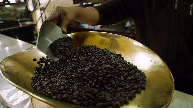 Coffee shop closeup shot seller weighting dark brown beans to sell on tray.