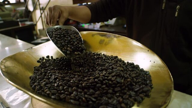 Coffee shop owner weighting dark brown coffee beans on scale to sell them.