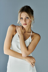 Naklejka premium A stunning woman with blonde hair wearing a white dress strikes a graceful pose against a grey background.
