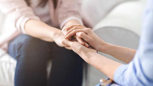 One woman offers comfort and reassurance by holding another woman hand during a heartfelt conversation in a cozy living room setting, cropped