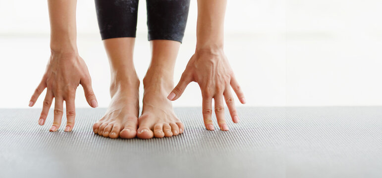 Cropped of woman is seen performing a stretching exercise in a studio, with hands touching feet on a yoga mat. The focus is on flexibility and balance during a morning routine, panorama, copy space