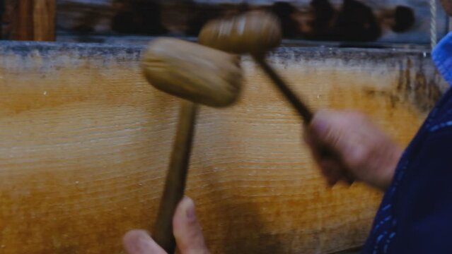 A man using two wooden mallets to beat a wooden semantron. A man using two wooden mallets to beat a wooden semantron