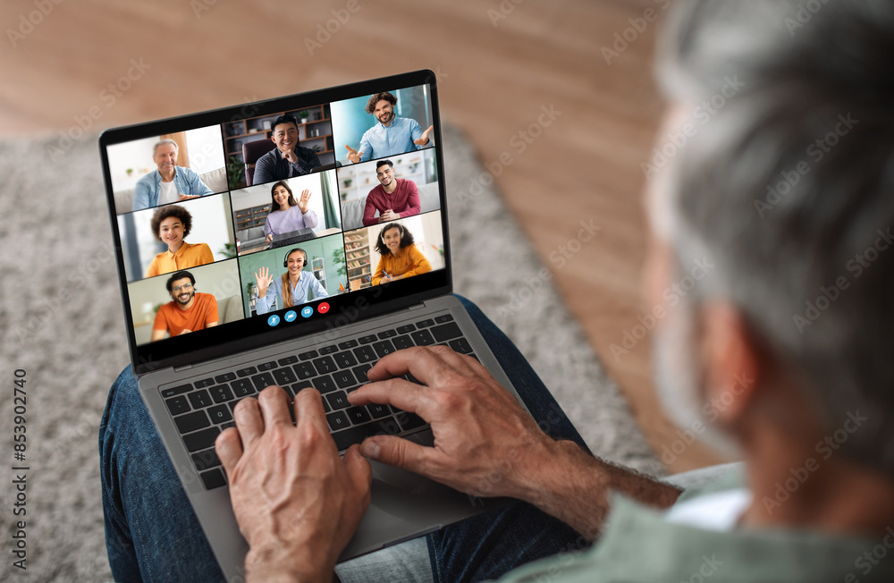 Poster mature man sits on a couch at home, using a laptop to participate in a virtual meeting. he is focuse