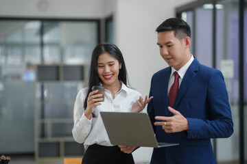 Two business professionals collaborating and discussing a project while looking at a laptop in a modern office environment.