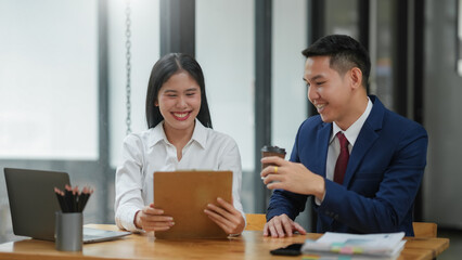 Two business professionals having a discussion in a modern office setting, sharing ideas while using a tablet and enjoying coffee.