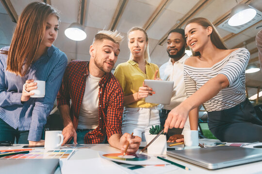 Diverse group of young professionals working together on design ideas, reviewing color options at a table in a bright, contemporary office space.