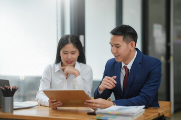 Two professionals discussing a business document at a desk in a modern office environment, focusing on collaboration and analysis.