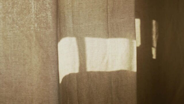 A soft breeze moves a curtain gently, creating a synchronized dance with sunlight patterns through a half-closed blind.