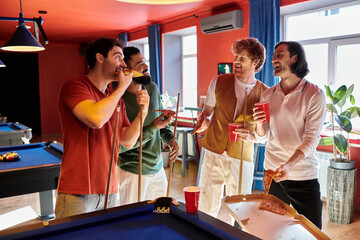 Friends gather around a pool table, enjoying pizza and drinks while taking a break from their game.