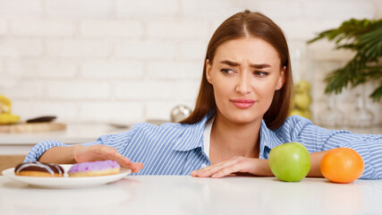 Dieting concept. Young Woman Choosing Between Fruits And Sweets