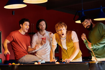 Friends play billiards, laughing and enjoying each others company.