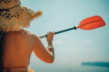 Woman in kayak back view. Happy woman with long hair in a swimsuit and hat floating in kayak on the...